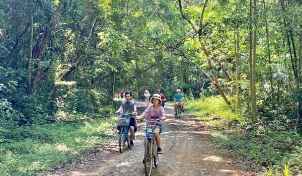 Des touristes font du vélo sur un sentier forestier du parc national de Cát Tiên, entourés par une végétation luxuriante.