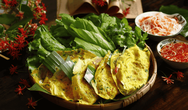 Une assiette de bánh xèo doré et croustillant, servi avec des herbes fraîches, des feuilles de salade et une sauce nuoc mam – un plat typique de la gastronomie vietnamienne d'été.
